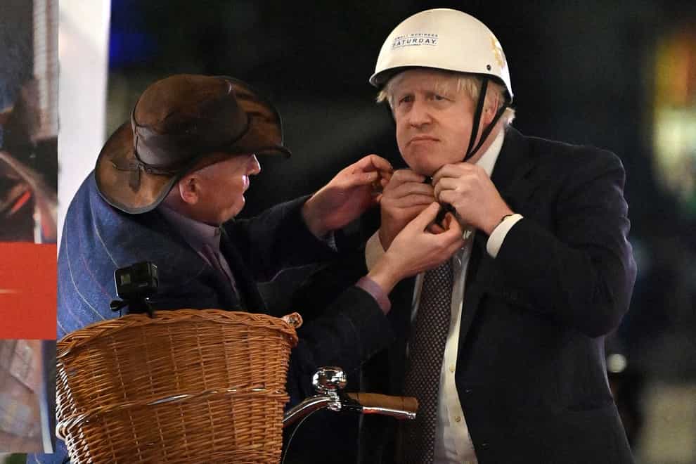 Prime Minister Boris Johnson receives help as he puts on a bicycle helmet before riding a bike as he visits a UK Food and Drinks market which has been set up in Downing Street, London. Picture date: Tuesday November 30, 2021.