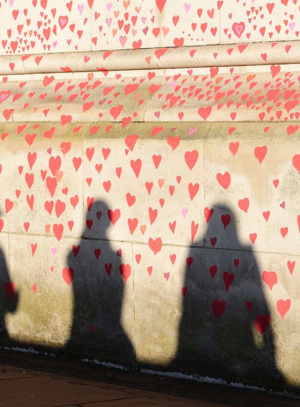 People are silhouetted against the COVID-19 Memorial Wall on the Embankment, central London (Ian West/PA)