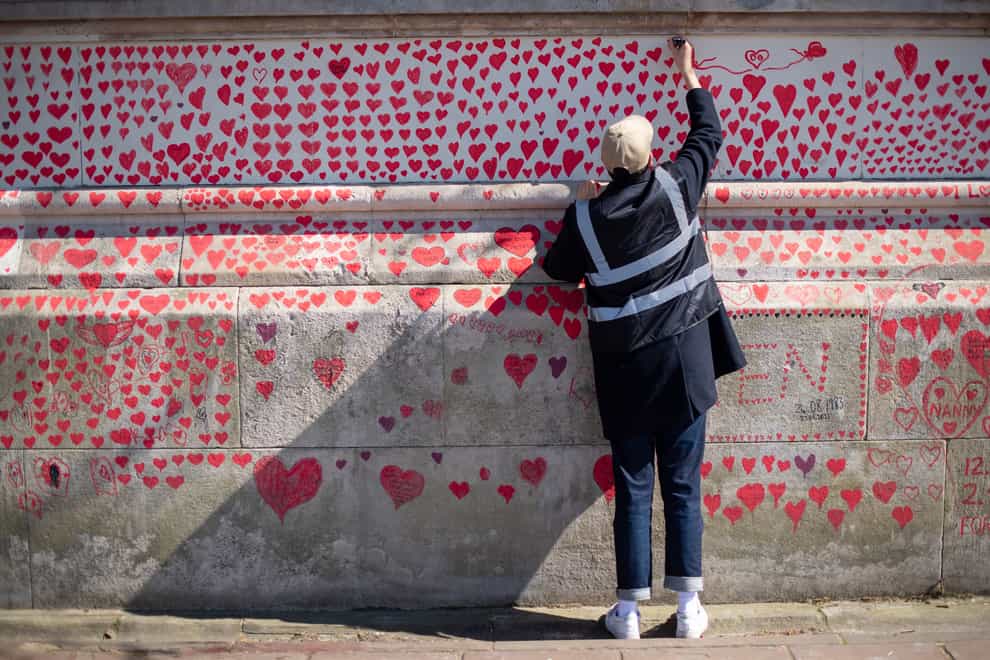 A volunteer adds hearts to the Covid memorial wall in Westminster, central London (Dominic Lipinski/PA)
