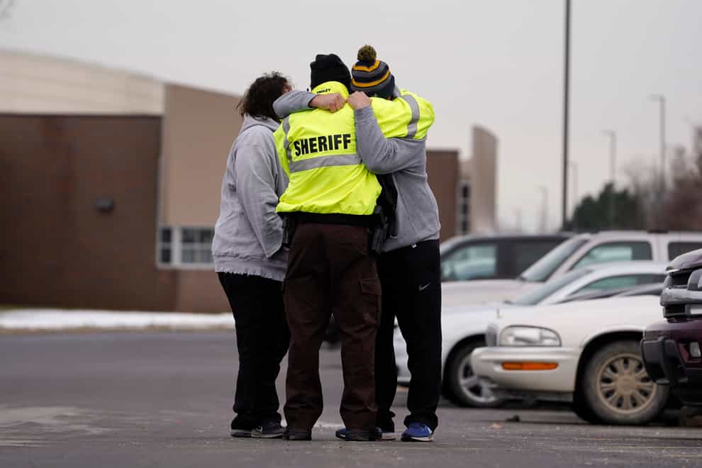 An Oakland County Sheriff’s deputy hugs family members of a student in the parking lot of Oxford High School in Oxford, Mich., Wednesday, Dec. 1, 2021. A 15-year-old sophomore opened fire at the school, killing several students and wounding multiple other people, including a teacher. (AP Photo/Paul Sancya)