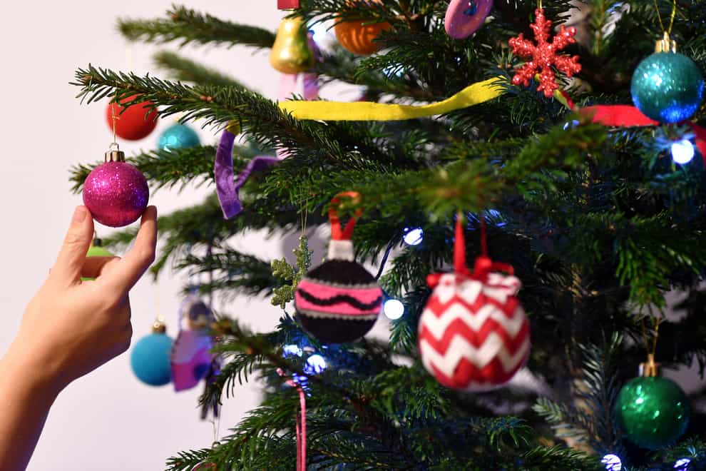 A woman adjusts a decoration on a Christmas tree.