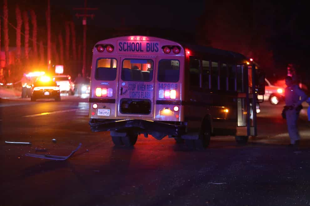 A police officer stands at the scene of a crash involving a school bus in Desert Hot Springs, Calif., on Thursday, Dec. 9, 2021. A child was killed when a car struck the school bus in Southern California and then plowed into a group of walking children. (Taya Gray/The Desert Sun via AP)