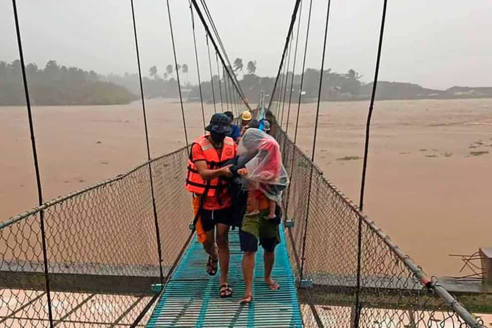 In this handout photo provided by the Philippine Coast Guard, rescuers assist residents cross a bridge as they are evacuated to higher grounds in Tubay town, Agusan del Norte, southern Philippines on Thursday, Dec. 16, 2021. Tens of thousands of people were being evacuated to safety in the southern and central Philippines as Typhoon Rai approached Thursday at a time when authorities were warning the public to avoid crowds after the first infections caused by the omicron strain of the coronavirus were reported in the country, officials said. (Philippine Coast Guard via AP)