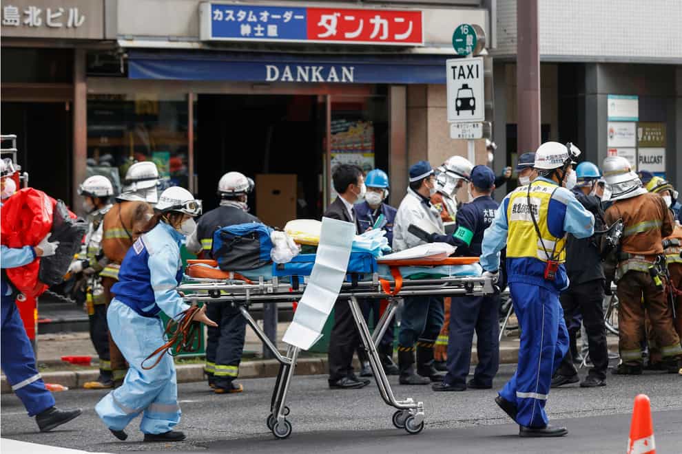 First responders carry a stretcher after a deadly fire at an eight-story building in a major business, shopping and entertainment district in Osaka, western Japan, Friday, Dec. 17, 2021. More than 20 people were feared dead after the fire broke out Friday in the building in Osaka, officials said, and police were investigating arson as a possible cause. (Yukie Nishizawa/Kyodo News via AP)