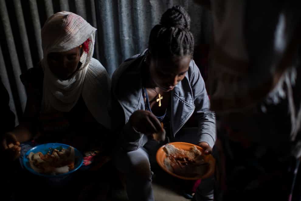 Displaced Tigrayan women sit in a metal shack to eat food donated by local residents at a reception centre for the internally displaced in Mekele, in the Tigray region (Ben Curtis/AP)