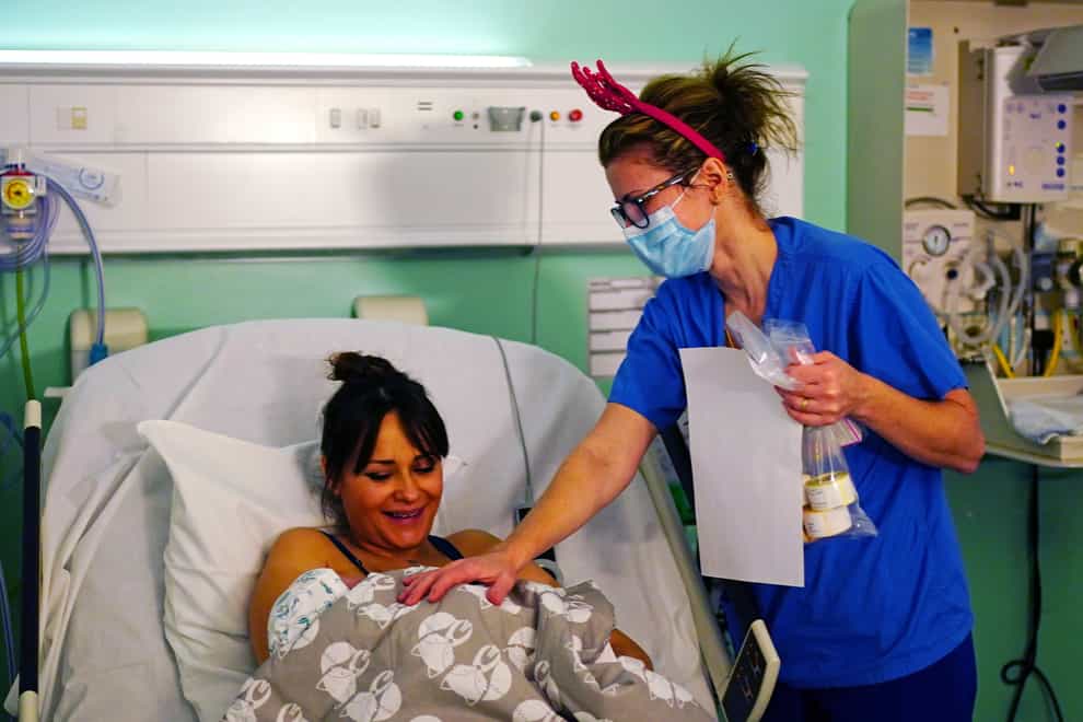 A medical staff member wearing a pair of festive antlers talks with a mother and her newborn baby on the labour ward at King’s College Hospital, in south east London (Victoria Jones/PA)