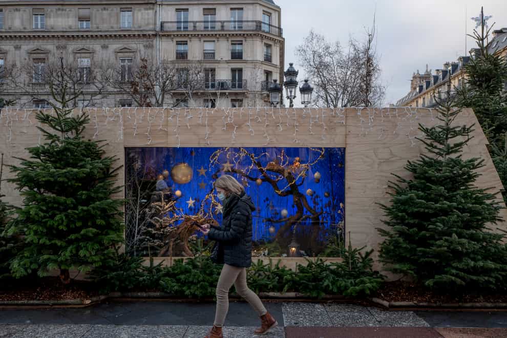 A woman wears a face mask to curb the spread of Covid-19 as she walks past Christmas decorations in Paris (Rafael Yaghobzadeh/AP)