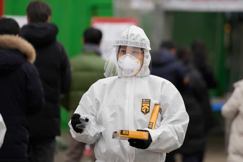 A medical worker wearing protective gear holds plastic gloves for visitors waiting in line for testing at a temporary screening clinic for the coronavirus in Seoul, South Korea (Lee Jin-man/AP)