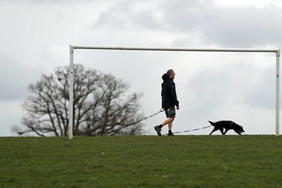 A man enjoys the mild weather as he walks his dog in Stoke Park, Guildford (Adam Davy/PA)