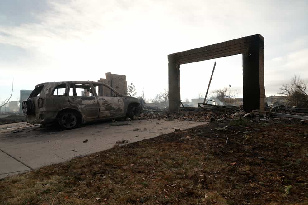A burnt out car sits in front of a smoldering home Friday, Dec. 31, 2021, in Superior, Colo. An estimated 580 homes, a hotel and a shopping center have burned and tens of thousands of people were evacuated in wind-fueled wildfires outside Denver, officials said Thursday evening. (AP Photo/Brittany Peterson)
