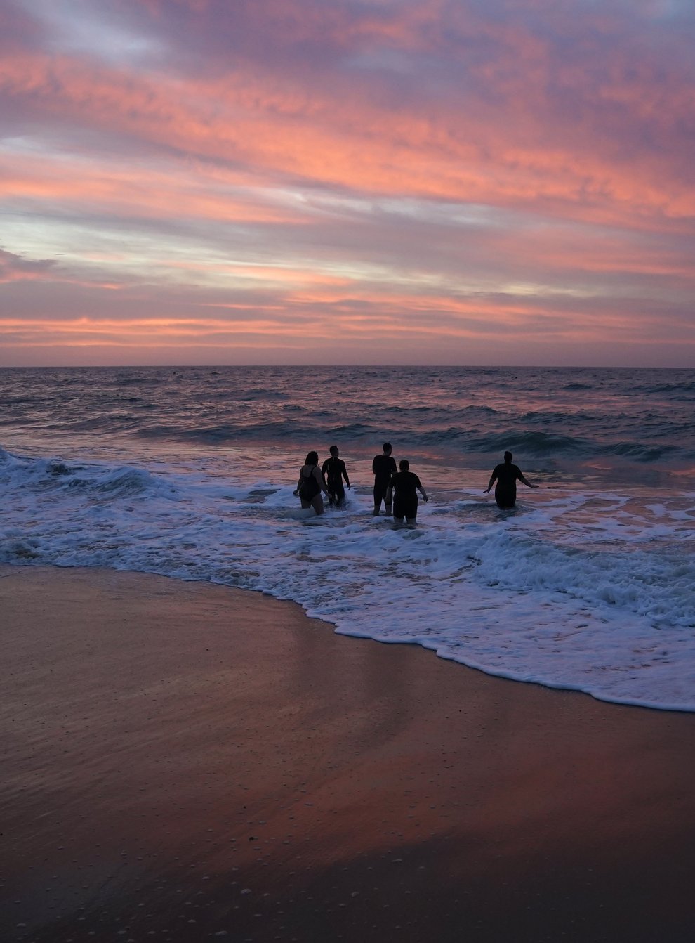 Swimmers make their way out to sea as the sun begins to rise over Boscombe beach in Dorset (Andrew Matthews/PA)