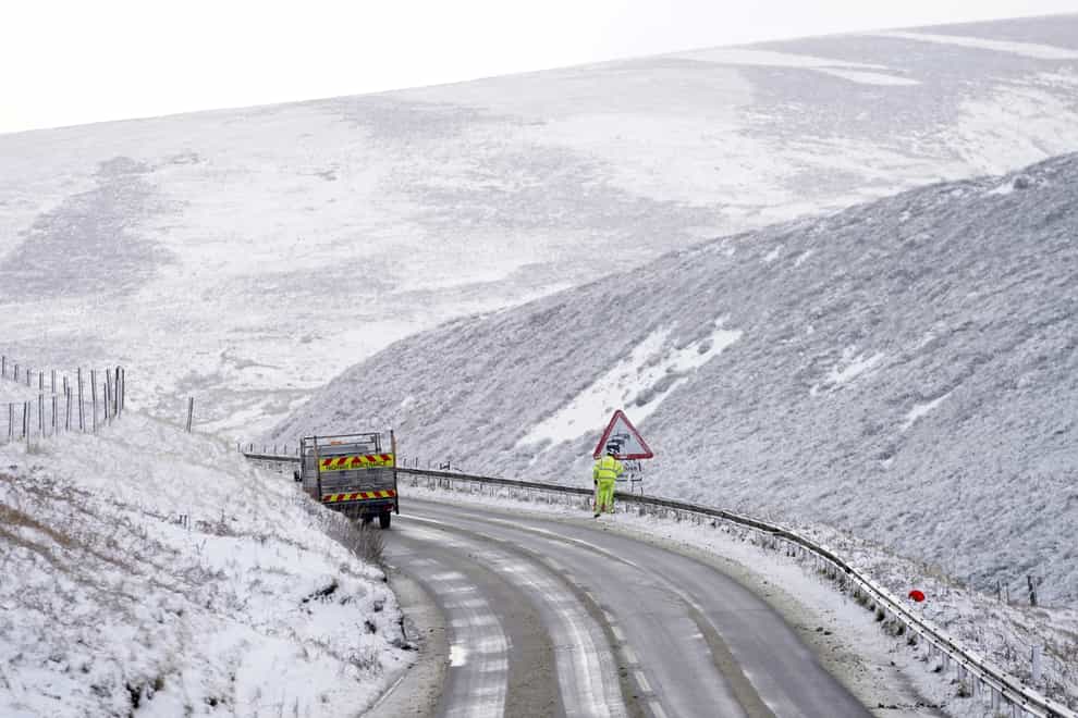 A highway maintenance worker clearing snow off a road sign on the A628 at Woodhead pass (Danny Lawson/PA)