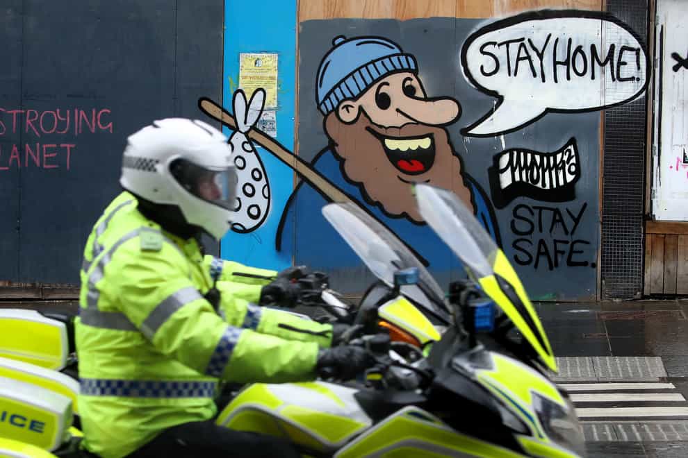 A police motorcyclist passes coronavirus related graffiti on a wall in Glasgow (Andrew Milligan/PA)