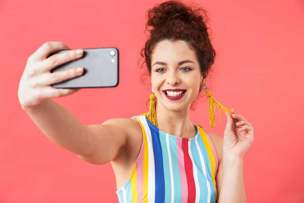 Smiling woman wearing colourful striped dress taking a selfie (Alamy/PA)