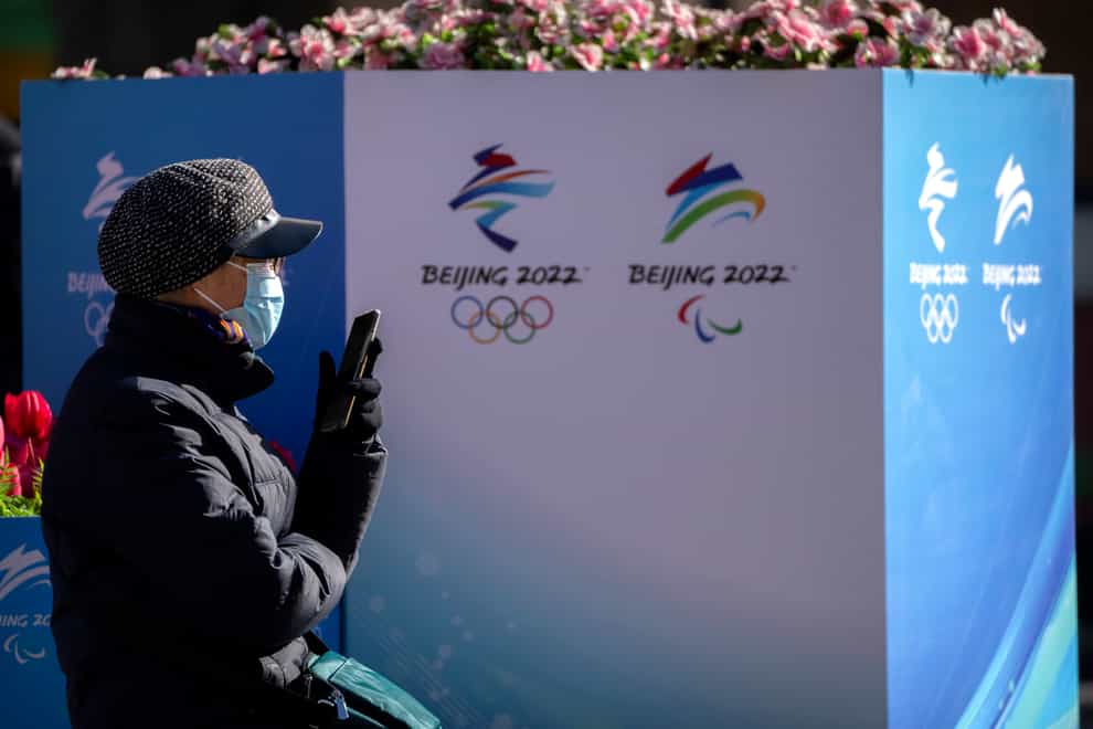 A woman wearing a face mask to protect against Covid-19 sits near landscaping decorated with the logos for the Beijing Winter Olympics and Paralympics on a pedestrian shopping street in Beijing (Mark Schiefelbein/AP)