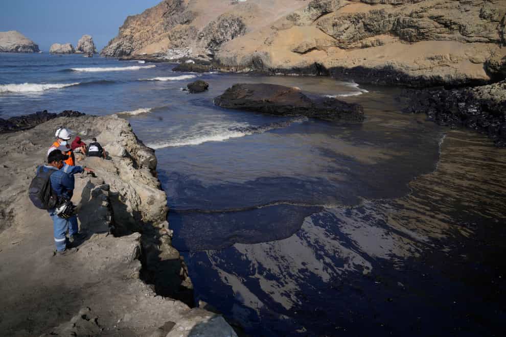 Workers look at the oil in the waters of Cavero Beach in Ventanilla, Callao, Peru (AP)