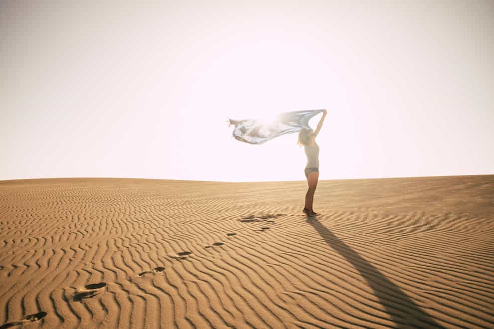 Standing woman against the sun on a desert dune (Alamy/PA)