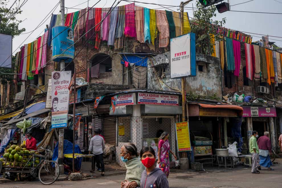 Commuters wearing masks walk past a cloth dyeing factory in Kolkata in India (Bikas Das/AP)