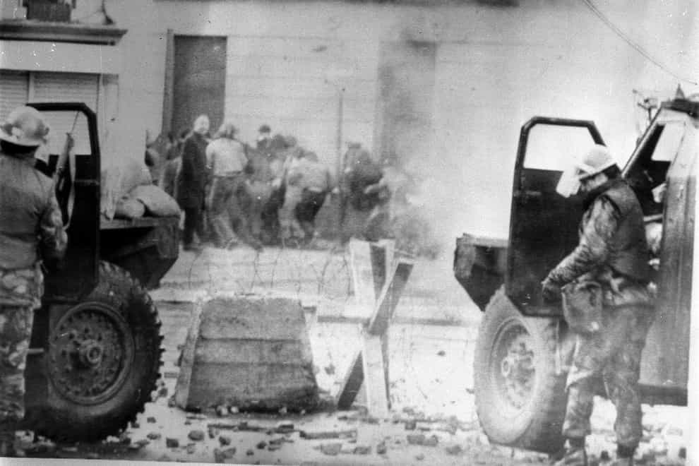 Soldiers take cover behind their armoured cars while dispersing rioters with CS gas in Londonderry (PA)