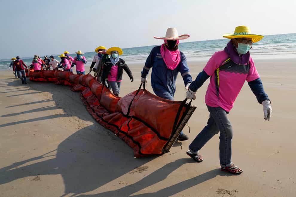 Workers drag an oil spill boom out onto Mae Ram Phueng Beach in hopes of containing any oil washing ashore from a recent spill off the coast of Rayong, eastern Thailand, Friday, Jan. 28, 2022. An oil slick off the coast of Thailand continued to expand Friday and was approaching beaches on the east coast, home to fragile coral and seagrass, officials said. (AP Photo/Sakchai Lalit)