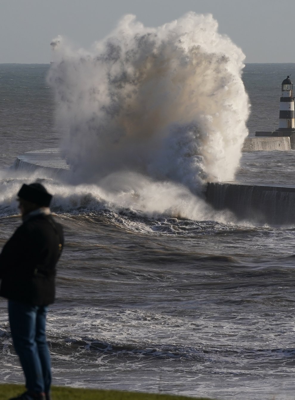 People watch as waves crash against the lighthouse in Seaham Harbour, County Durham (PA)