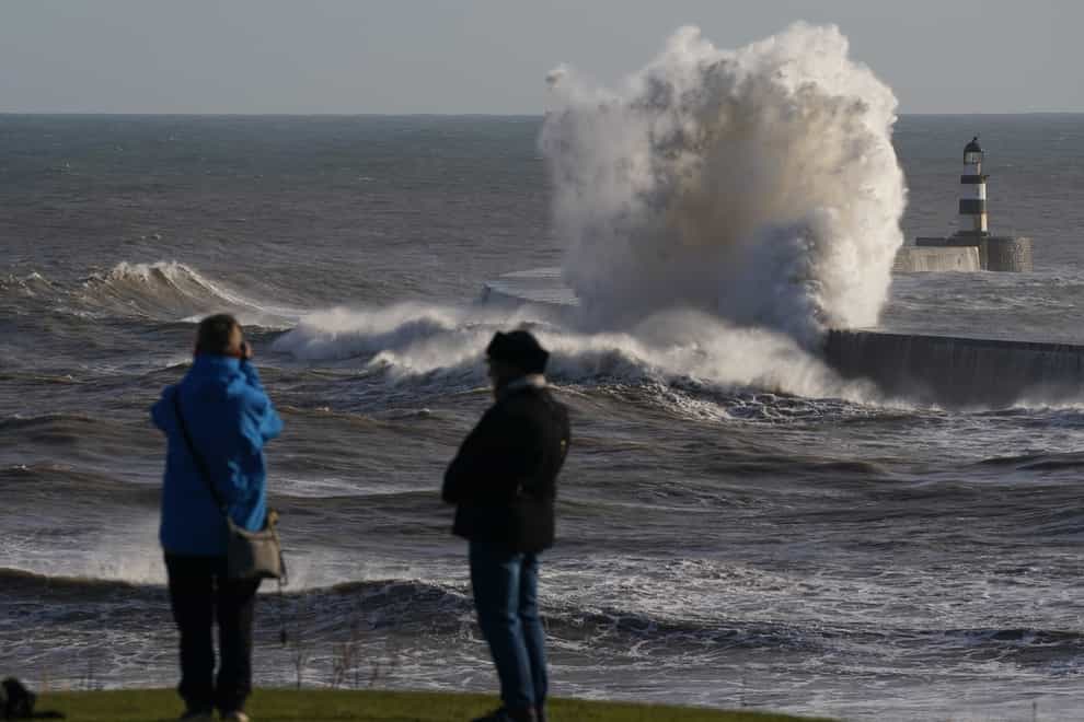 People watch as waves crash against the lighthouse in Seaham Harbour, County Durham (PA)