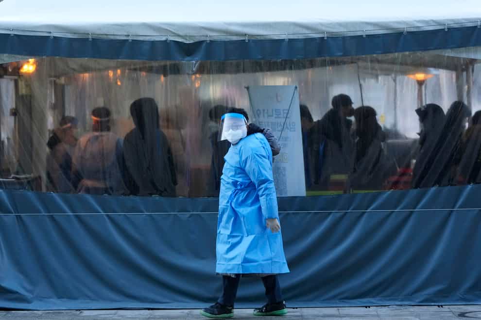 A medical worker passes by people as they wait for their coronavirus tests in Seoul, South Korea (Ahn Young-joon/AP)