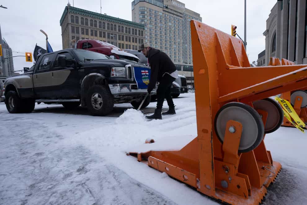 A protester shovels snow from around protest vehicles, Thursday, Feb. 3, 2022 in Ottawa (AP)