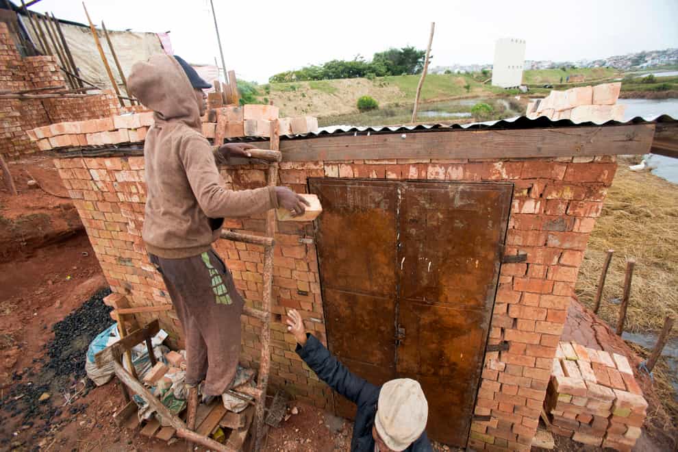 A man weighs down the roof of his home with bricks to stop it from flying away (Alexander Joe/AP)