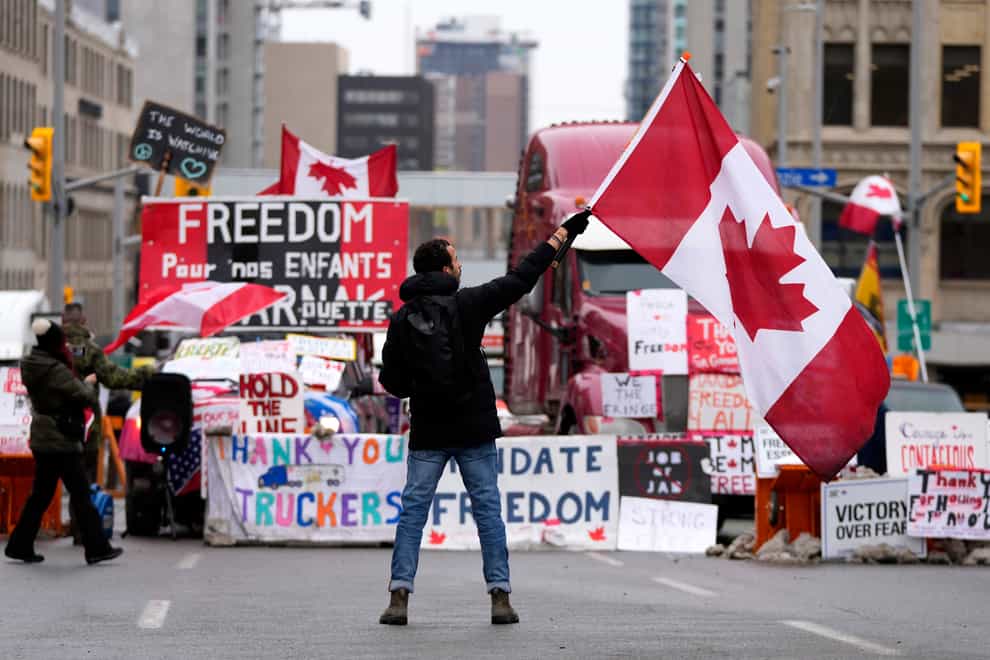 A protester waves a Canadian flag in front of parked vehicles on Rideau Street (The Canadian Press/AP)