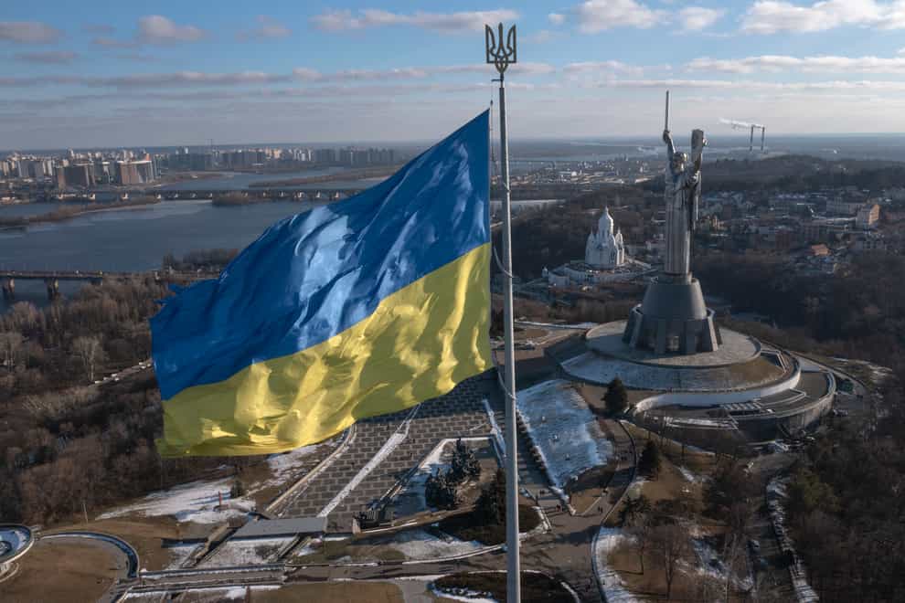 A view of Ukraine’s national flag waves above the capital with the Motherland Monument on the right, in Kyiv Sunday, Feb. 13, 2022. Some airlines have halted or diverted flights to Ukraine amid heightened fears that an invasion by Russia is imminent despite intensive weekend talks between the Kremlin and the West. (AP Photo/Efrem Lukatsky)