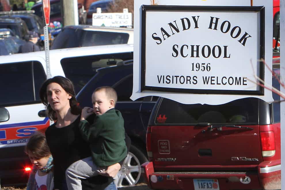 FILE — A parent walks away from the Sandy Hook Elementary School with her children following a shooting at the school in Newtown, Conn., Dec. 14, 2012. The families of nine victims of the Sandy Hook Elementary School shooting have agreed to a settlement of a lawsuit against the maker of the rifle used to kill 20 first graders and six educators in 2012, according to a court filing, Tuesday, Feb. 15, 2022. (Frank Becerra Jr./The Journal News via AP)
