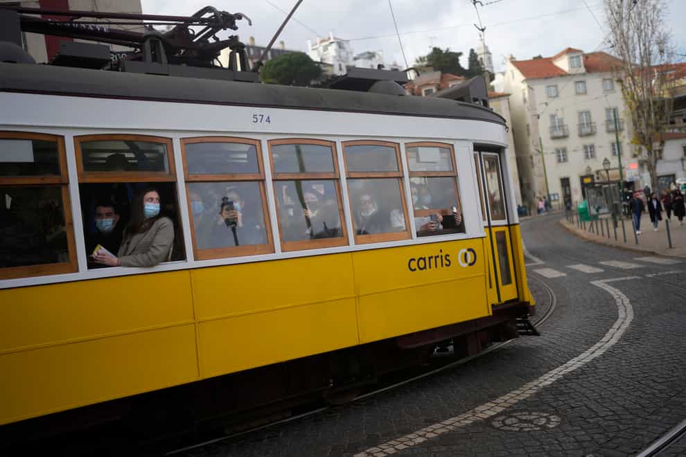 Passengers wearing face masks against the spread of coronavirus take pictures from a tram driving through the Alfama neighbourhood in Lisbon (Armando Franca/AP)
