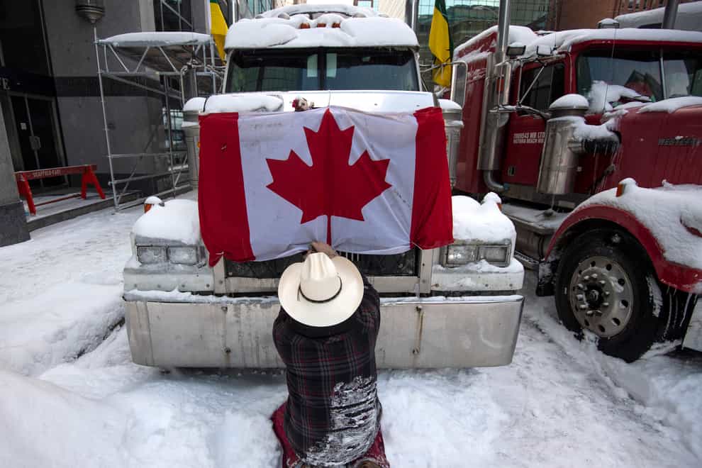 A trucker removes a flag of Canada from the hood of their vehicle as truckers prepare to drive away after participating in a blockade on Metcalfe Street in Ottawa, Ontario (Justin Tang/The Canadian Press via AP)