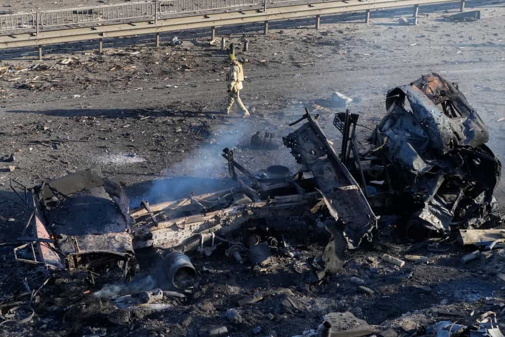 A Ukrainian soldier walks past debris of a burning military truck (AP)