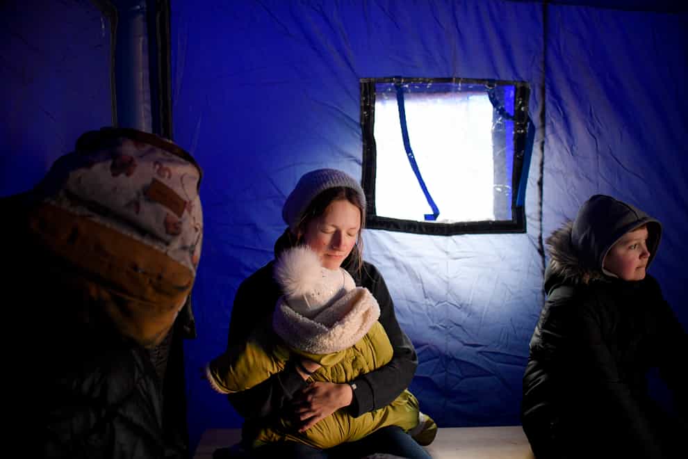 A refugee fleeing the conflict from neighbouring Ukraine holds her baby as she sits in a tent at the Romanian-Ukrainian border, in Siret, Romania (Andreea Alexandru/AP)