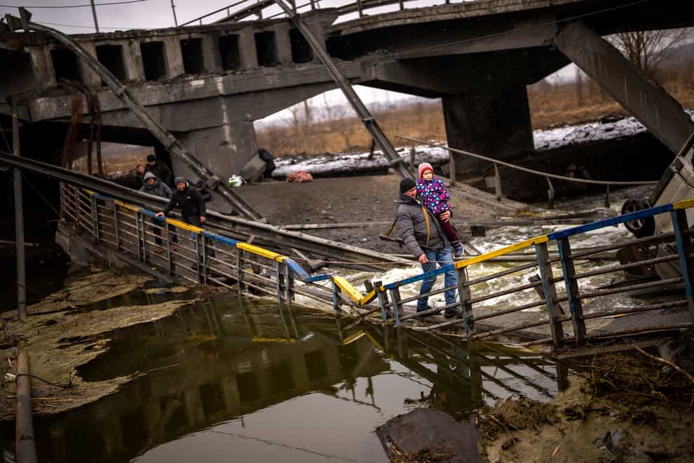 Local militiaman Valery, 37, carries a child as he helps a fleeing family across a bridge destroyed by artillery, on the outskirts of Kyiv, Ukraine, on Wednesday, March 2 2022 (AP Photo/Emilio Morenatti)