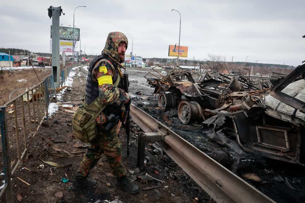 An armed man stands by the remains of a Russian military vehicle in Bucha, close to the capital Kyiv (Serhii Nuzhnenko/AP)