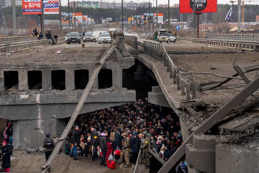 Ukrainians crowd under a destroyed bridge as they try to flee crossing the Irpin river in the outskirts of Kyiv, Ukraine (AP)
