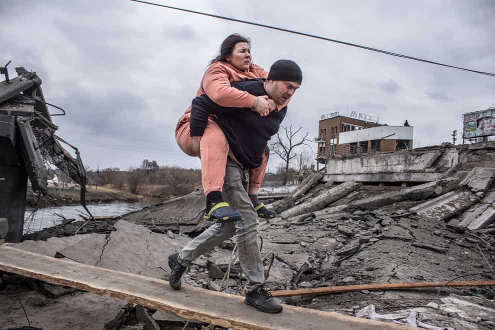 A man carries a woman as they cross an improvised path while fleeing the town of Irpin, Ukraine, on Sunday March 6 2022(Oleksandr Ratushniak/AP)