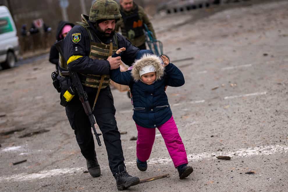 A Ukrainian police officer runs while holding a child as the artillery echoes nearby on the outskirts of Kyiv (AP)