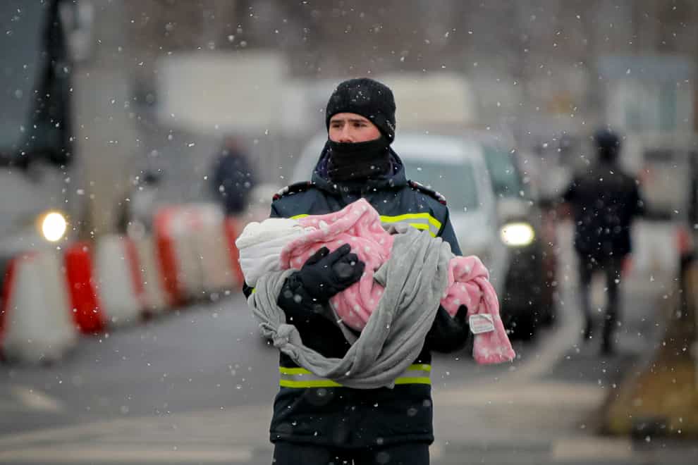 A firefighter holds the baby of a refugee fleeing the conflict from neighbouring Ukraine at the Romanian-Ukrainian border in Siret, Romania (Andreea Alexandru/AP)