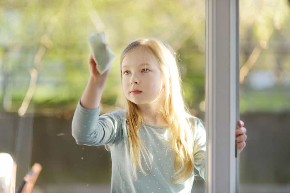 2BYC65H Cute young girl cleaning a window with paper cloth. Child helping with everyday chores. Tidying up with kids.