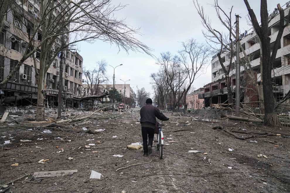 A man walks with a bicycle in a street damaged by shelling in Mariupol, Ukraine (Evgeniy Maloletka/AP)