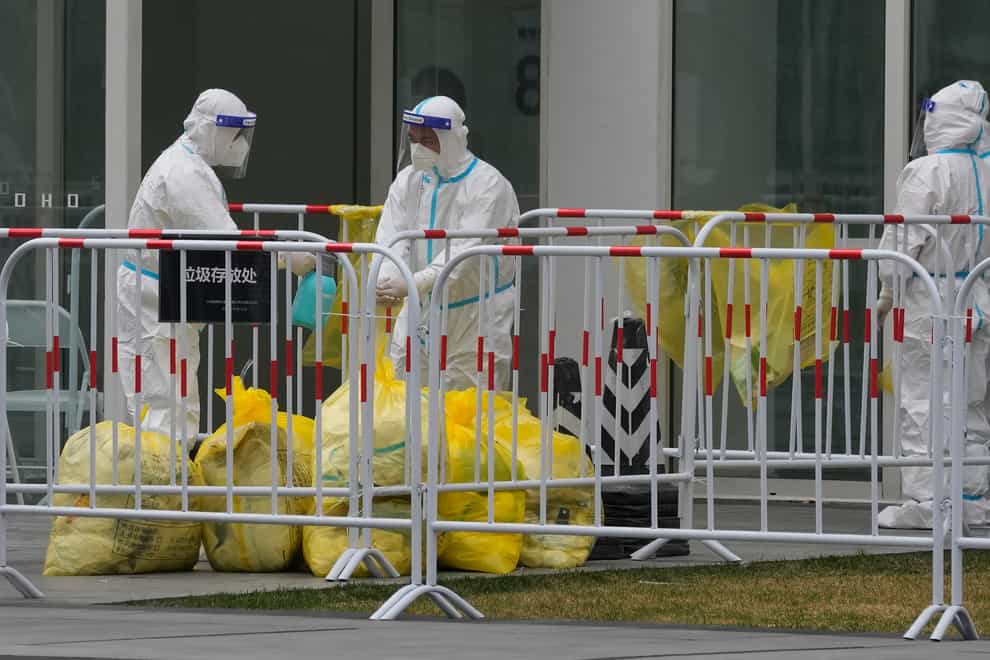 Workers disinfect each other after handling rubbish bags outside an office building in Beijing that was closed off after a case of coronavirus was detected on Sunday (Ng Han Guan/AP)