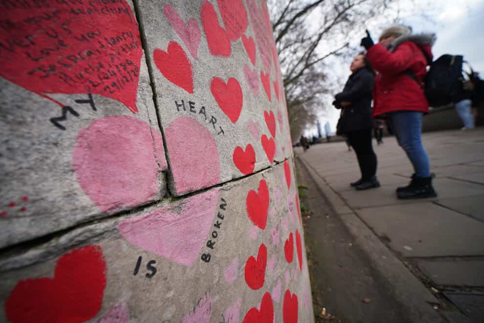 People stop to look at tributes on the Covid memorial wall in Westminster, central London (Yui Mok/PA)