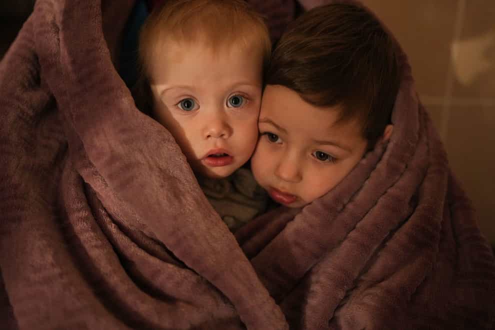 The children of medical workers warm themselves in a blanket as they wait for their relatives in a hospital in Mariupol, Ukraine (Evgeniy Maloletka/AP)