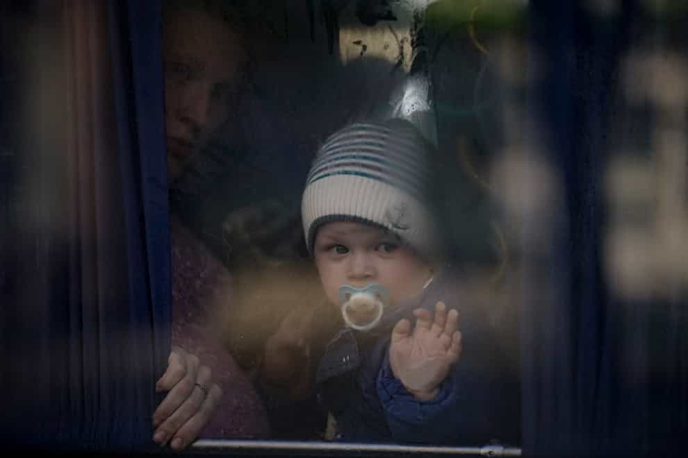 A refugee woman holds a baby while waiting on a bus for Ukrainian police to check papers and belongings (Vadim Ghirda/AP)