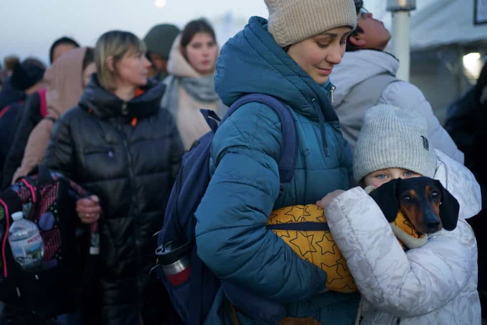 A young girl from Ukraine holds her dog as she waits with her mother for a bus to refuge accommodation after they crossed the border into Medyka, Poland (Victoria Jones/PA)