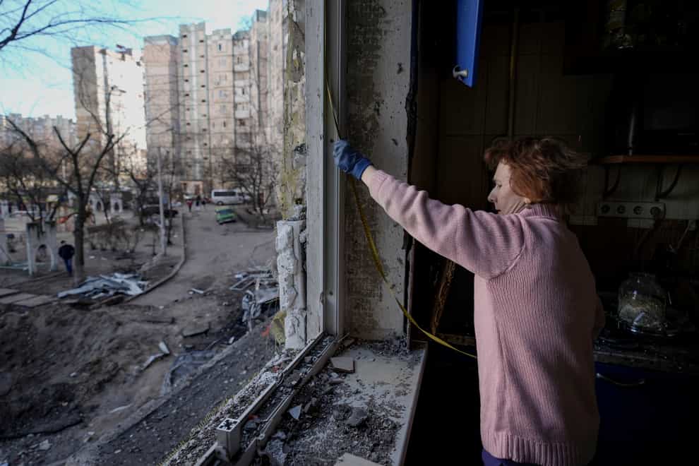 A woman measures a window before covering it with plastic sheets in a building damaged by a bombing (Vadim Ghirda/AP)